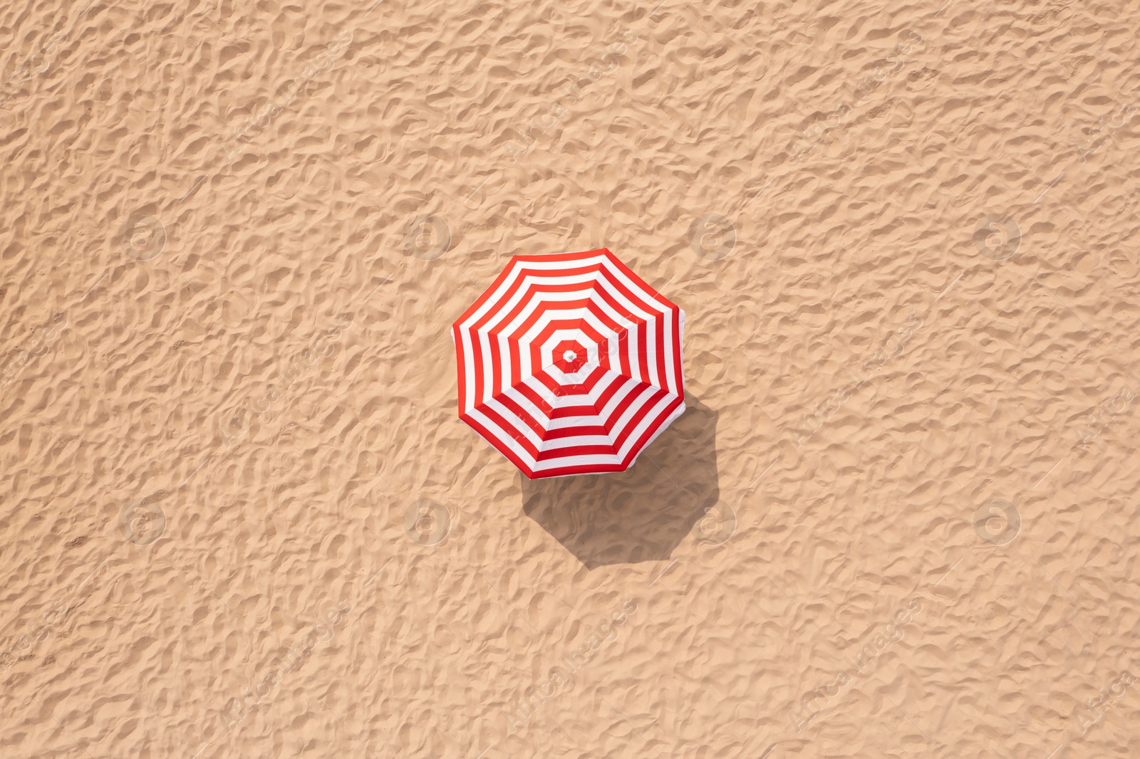 Image of Striped beach umbrella on sandy coast, aerial view