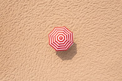 Image of Striped beach umbrella on sandy coast, aerial view