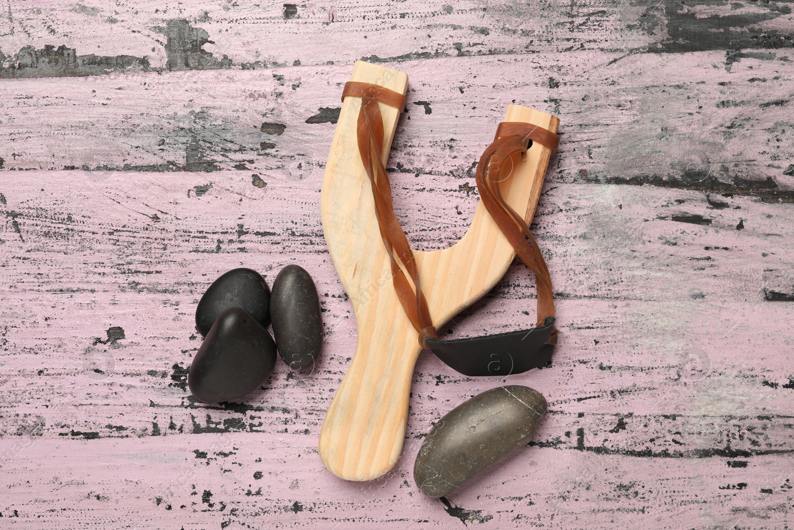 Photo of Slingshot with stones on old pink wooden background, flat lay