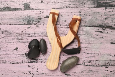 Slingshot with stones on old pink wooden background, flat lay