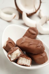 Delicious milk chocolate candy bars with coconut filling in bowl on white table, closeup. Space for text