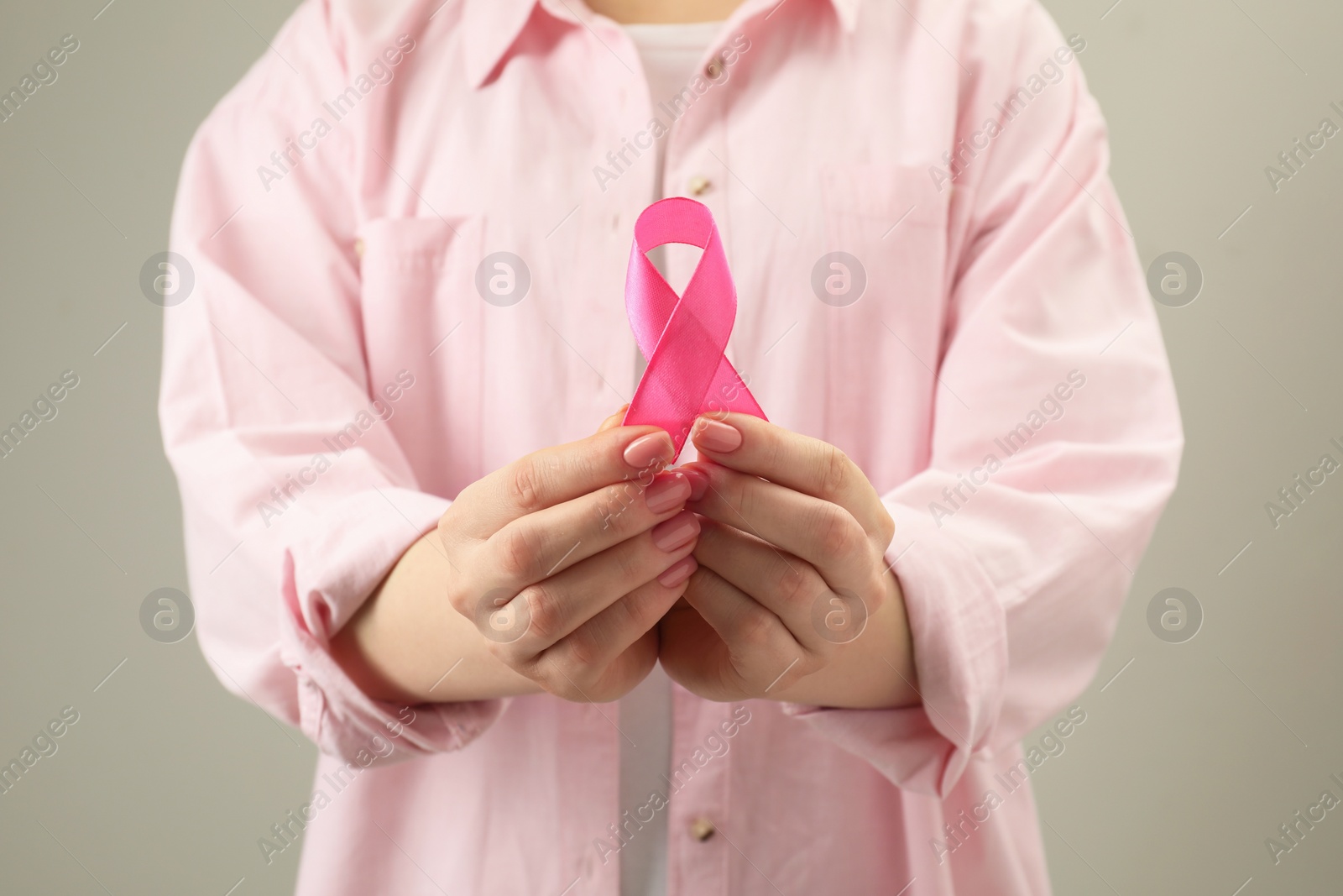 Photo of Woman with pink ribbon on light grey background, closeup. Breast cancer awareness