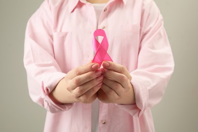 Photo of Woman with pink ribbon on light grey background, closeup. Breast cancer awareness