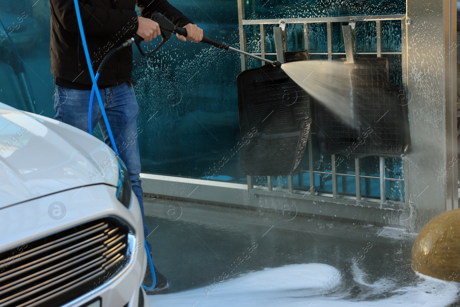 Photo of Man cleaning auto mats with high pressure water jet at self-service car wash, closeup