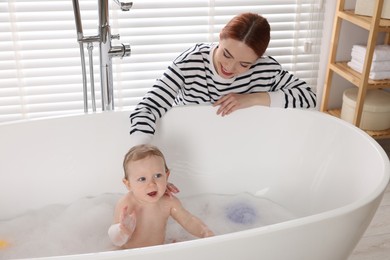 Mother washing her little baby in tub at home