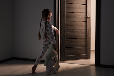 Girl in pajamas with toy bunny sleepwalking indoors at night
