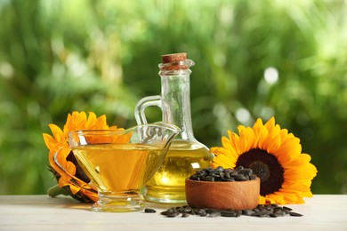 Photo of Sunflower cooking oil, seeds and yellow flowers on white wooden table outdoors
