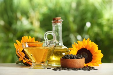 Sunflower cooking oil, seeds and yellow flowers on white wooden table outdoors