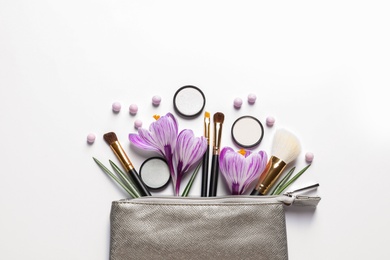 Makeup products, flowers and cosmetic bag on white background, top view