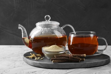 Photo of Aromatic licorice tea, dried sticks of licorice root and powder on light gray textured table