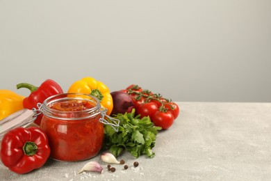 Glass jar of delicious canned lecho and fresh ingredients on light grey table. Space for text