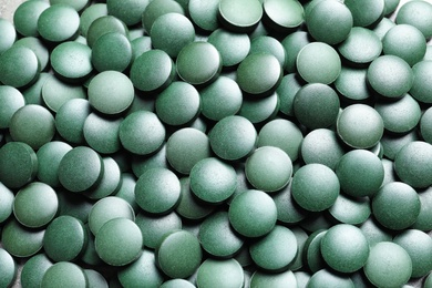 Photo of Green spirulina pills as background, closeup view