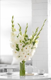 Photo of Vase with beautiful white gladiolus flowers on wooden table in living room