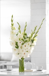 Vase with beautiful white gladiolus flowers on wooden table in living room