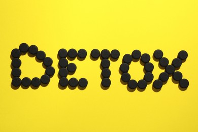 Word Detox made of activated charcoal pills on yellow background, flat lay. Potent sorbent