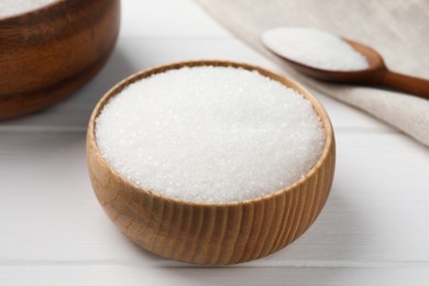 Granulated sugar in bowl on white wooden table, closeup