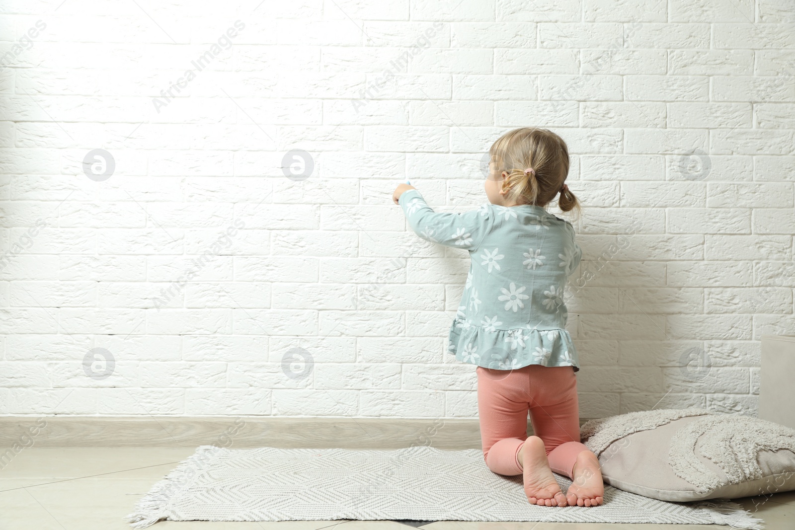 Photo of Little girl drawing on white brick wall indoors, back view and space for text. Child`s art