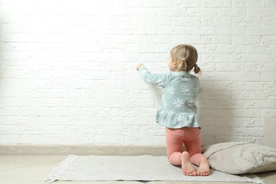 Little girl drawing on white brick wall indoors, back view and space for text. Child`s art