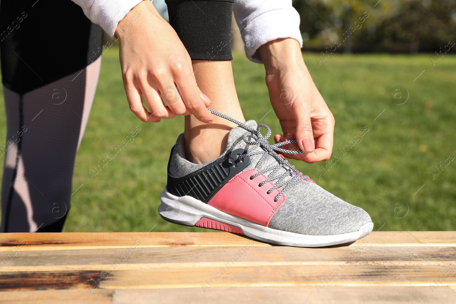 Image of Sporty woman tying shoelaces in park on sunny morning, closeup