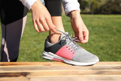 Sporty woman tying shoelaces in park on sunny morning, closeup