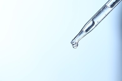 Dripping liquid from pipette on light blue background, closeup. Space for text