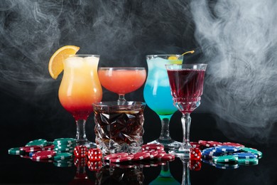 Photo of Casino chips, dice and alcohol drinks on dark background with smoke