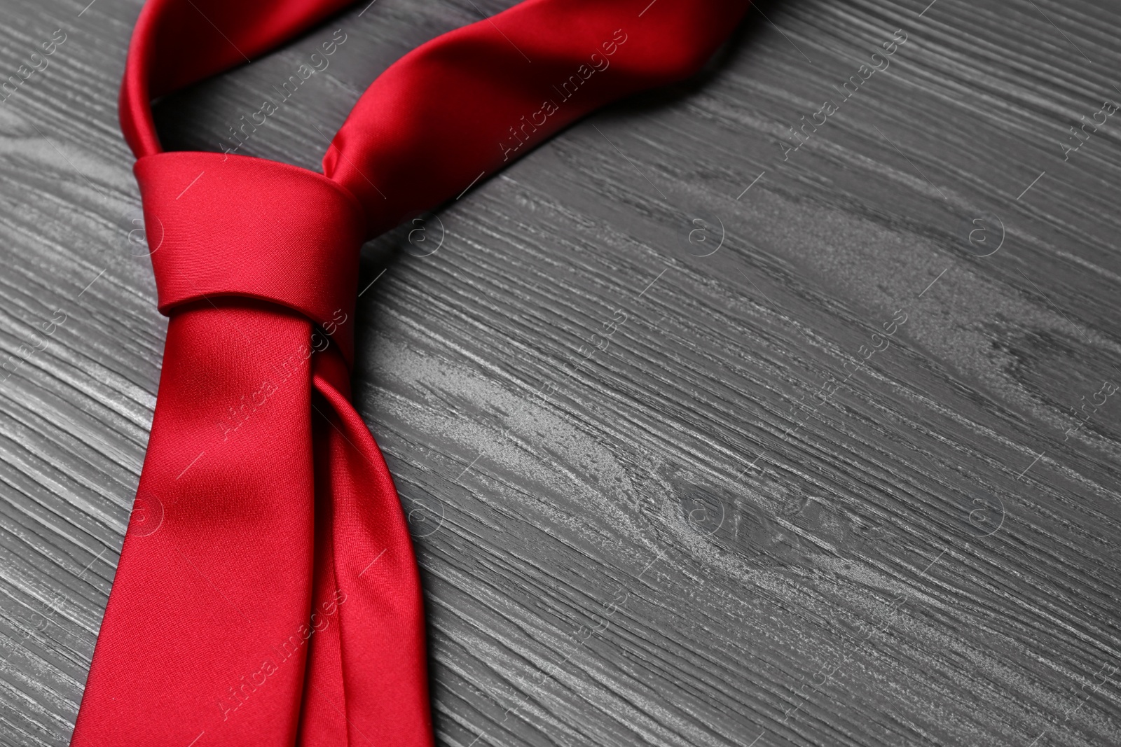 Photo of Stylish red silk necktie on dark grey wooden table, space for text