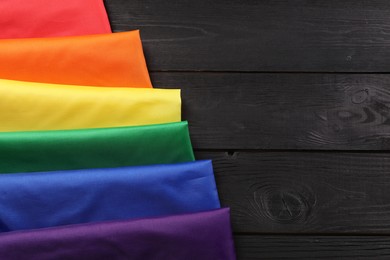 Photo of Rainbow LGBT flag on black wooden background, top view. Space for text