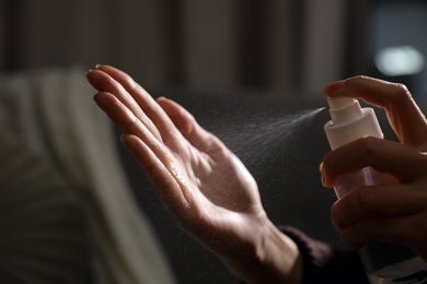 Photo of Woman spraying antiseptic onto hand against blurred background, closeup