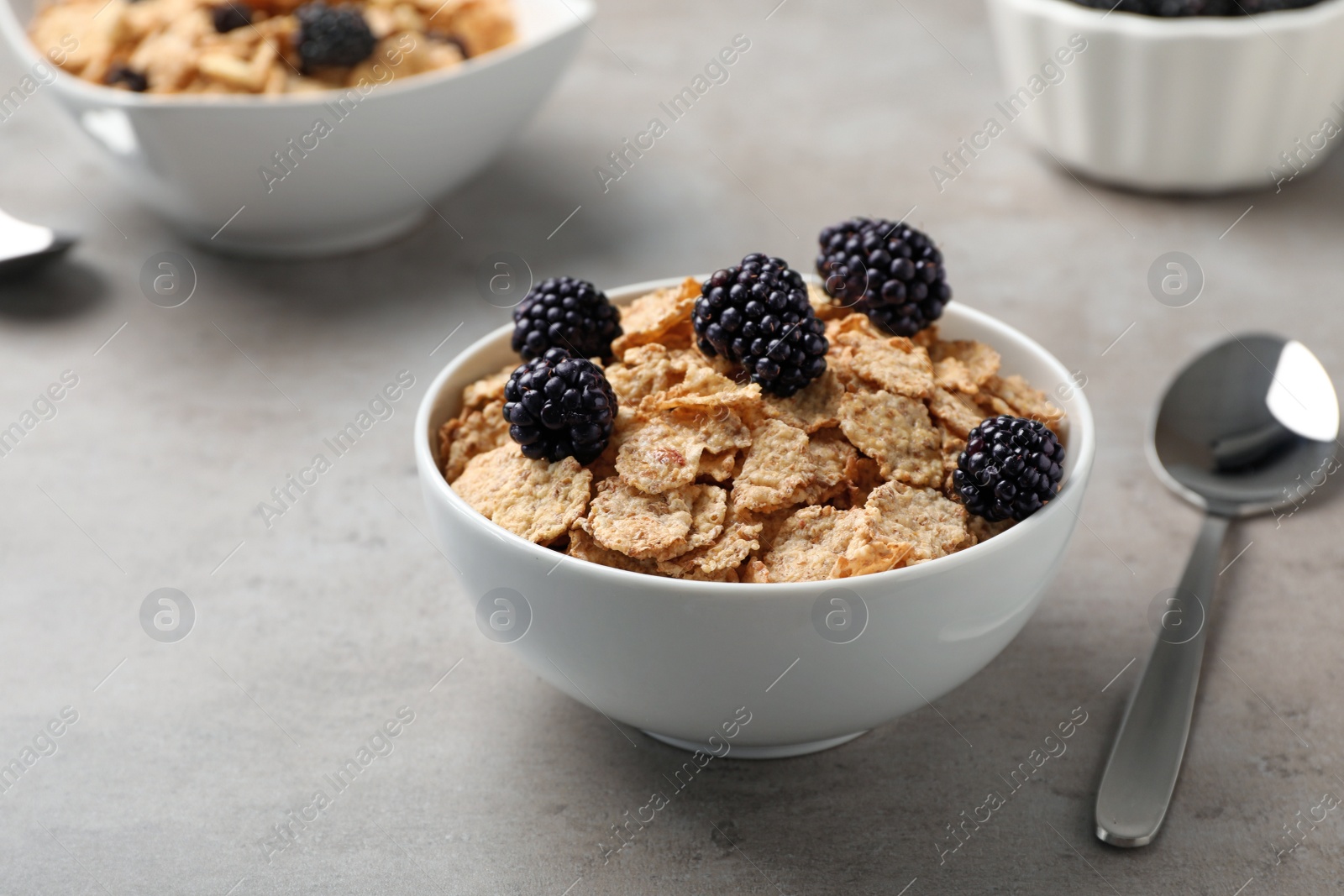 Photo of Bowl with cornflakes and blackberries on gray table. Whole grain cereal for breakfast