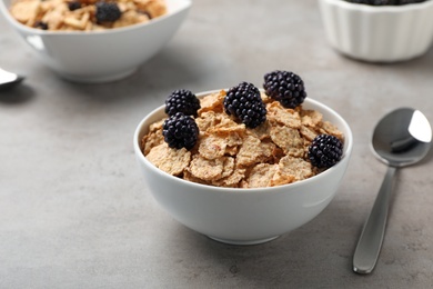 Photo of Bowl with cornflakes and blackberries on gray table. Whole grain cereal for breakfast