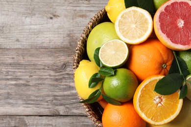 Different fresh citrus fruits and leaves in wicker basket on wooden table, top view. Space for text