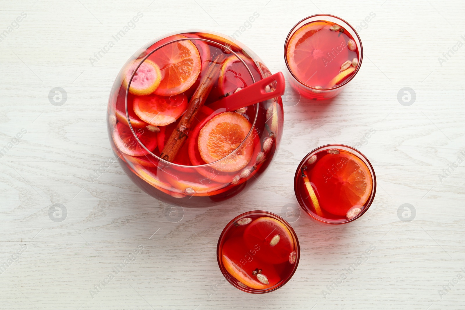 Photo of Glasses and bowl of delicious aromatic punch drink on white wooden table, flat lay