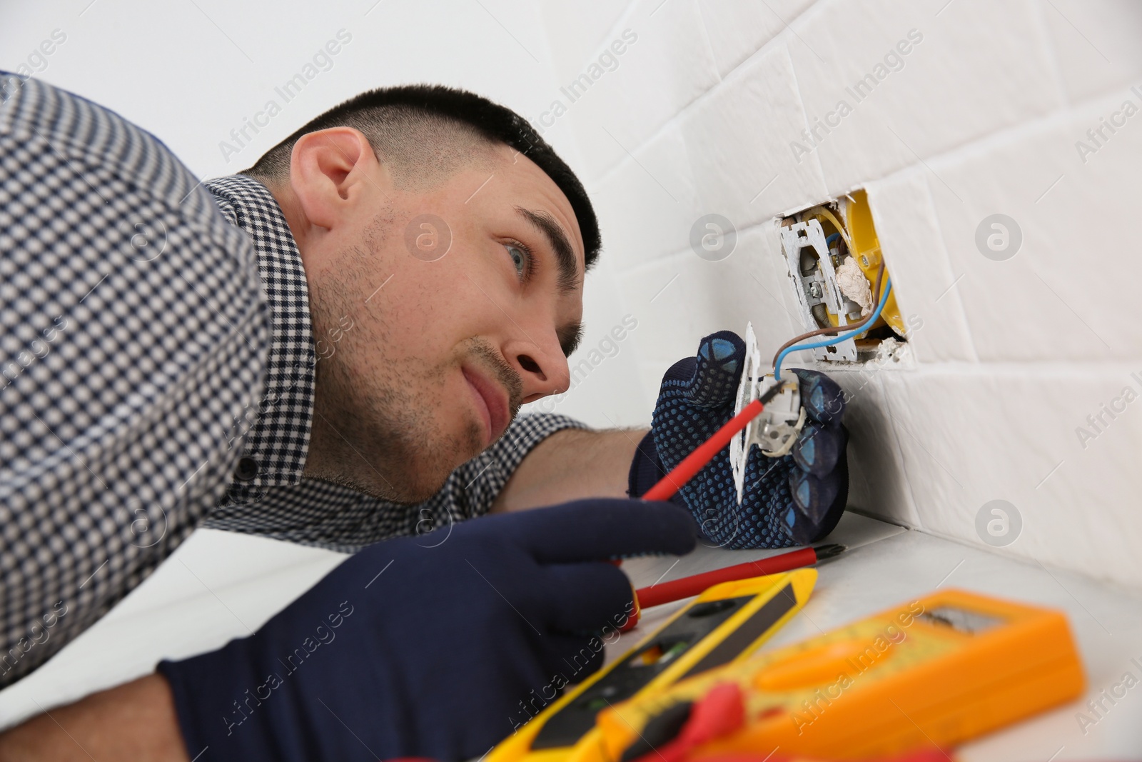 Photo of Electrician with screwdriver repairing power socket indoors