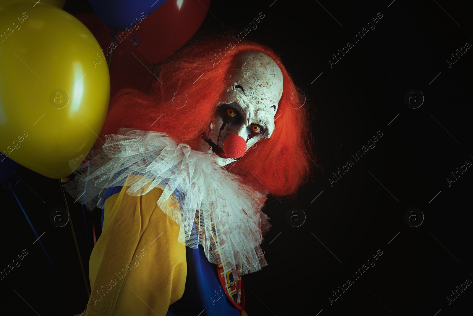 Photo of Terrifying clown with air balloons on black background, space for text. Halloween party costume