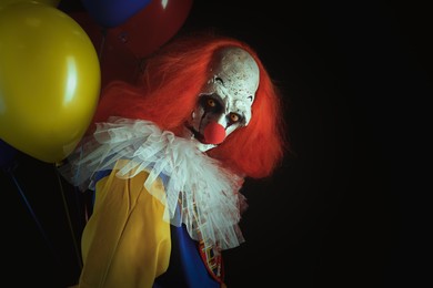 Photo of Terrifying clown with air balloons on black background, space for text. Halloween party costume
