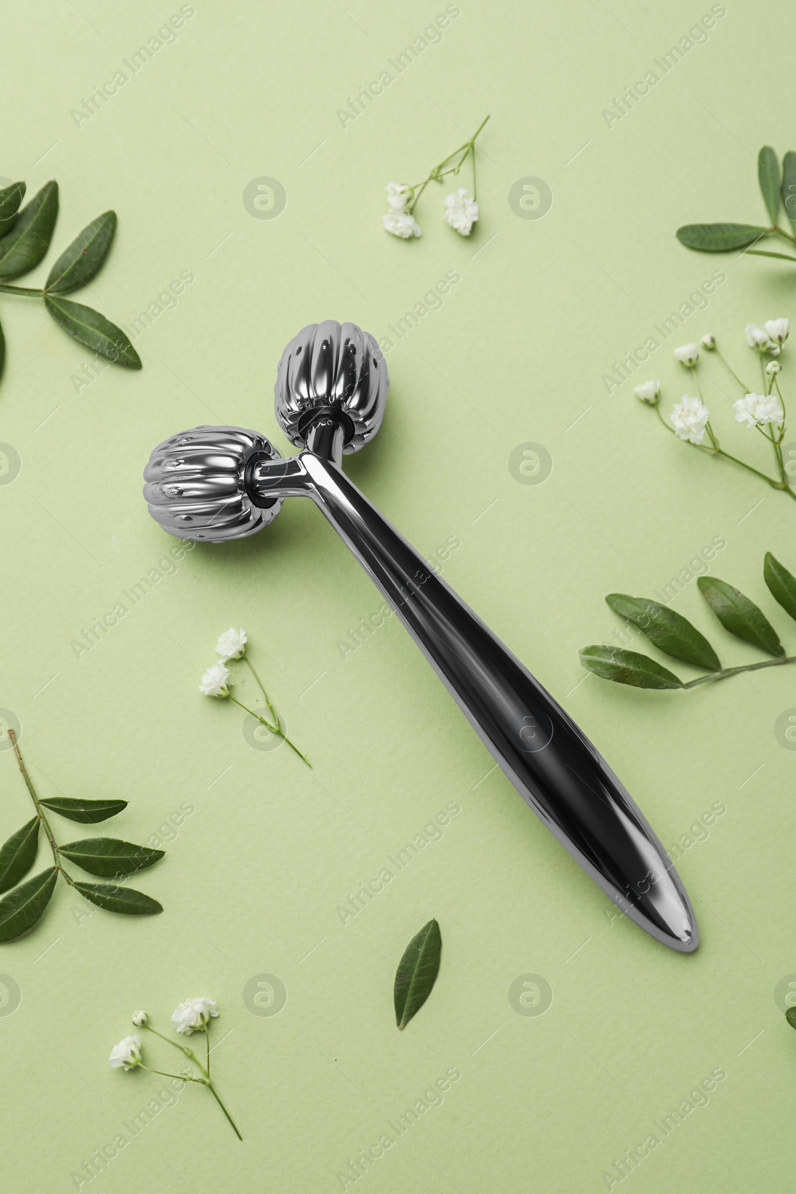 Photo of Metal face roller and flowers on green background, flat lay