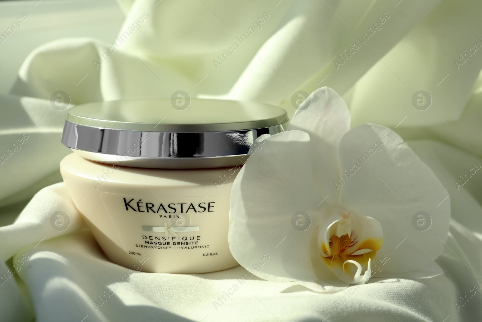 Photo of MYKOLAIV, UKRAINE - SEPTEMBER 07, 2021: Kerastase hair care mask and beautiful orchid flower on white fabric