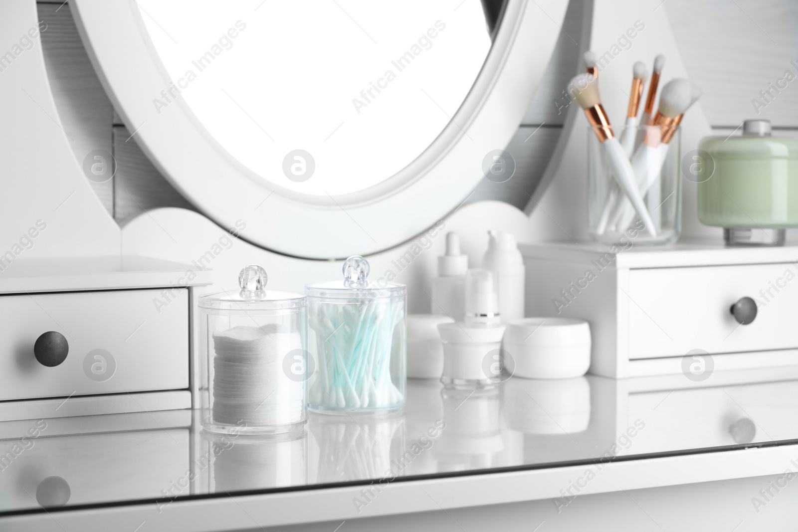 Photo of Containers with cotton swabs and pads near cosmetic products on dressing table indoors