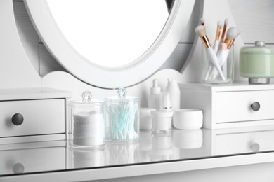 Photo of Containers with cotton swabs and pads near cosmetic products on dressing table indoors