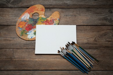 Photo of Blank canvas, brushes and palette on wooden table, flat lay. Space for text