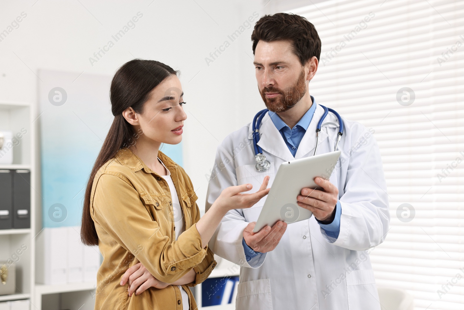 Photo of Doctor with tablet consulting patient during appointment in clinic