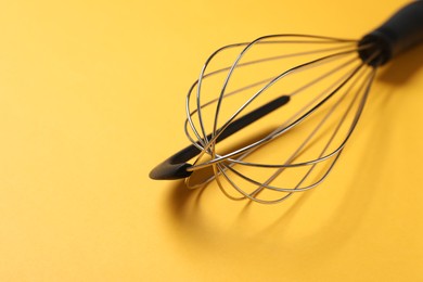 Photo of Metal whisk on yellow background, closeup. Space for text