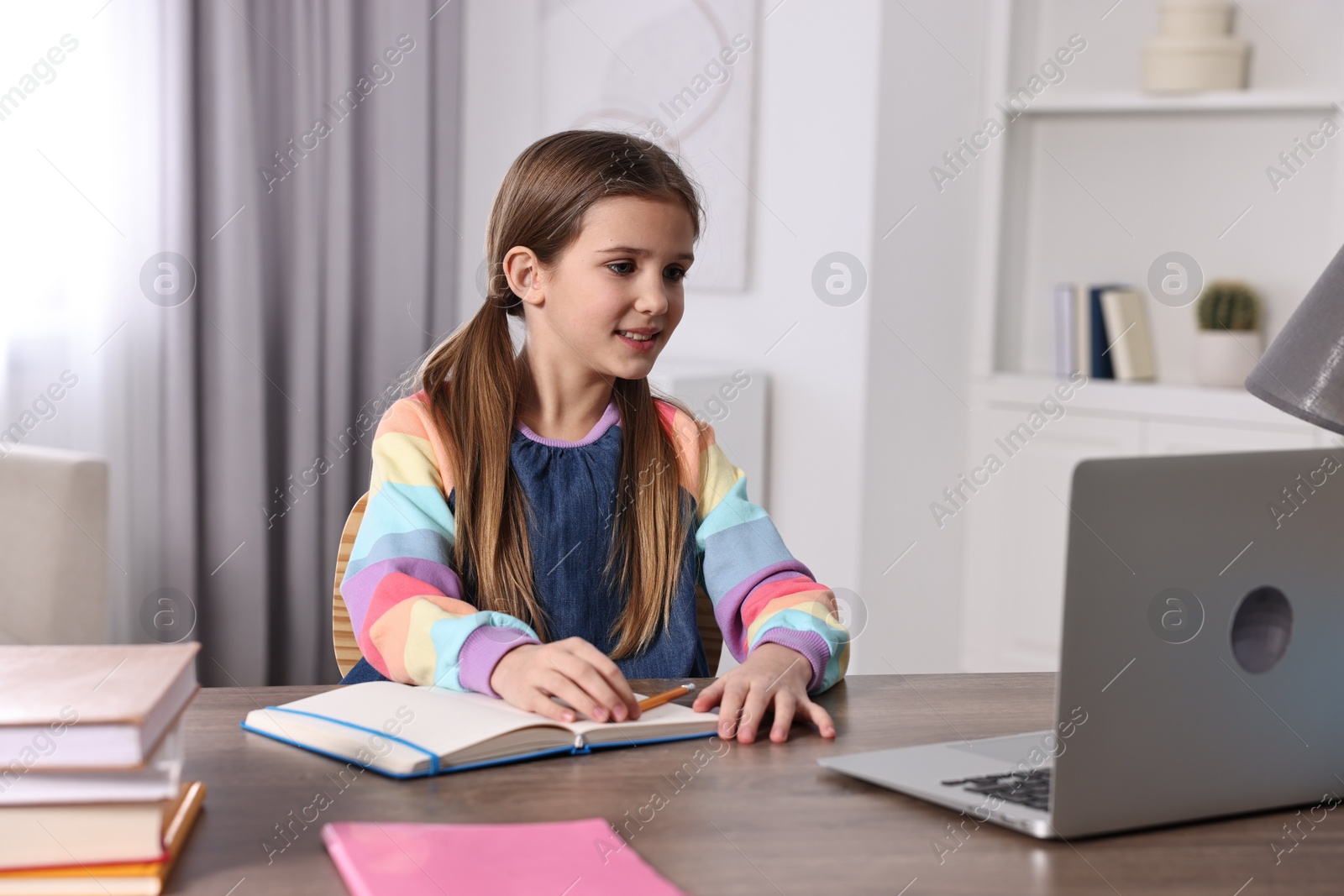 Photo of E-learning. Cute girl using laptop during online lesson at table indoors