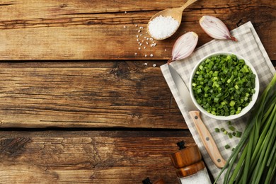 Photo of Chopped green onion in bowl on wooden table, flat lay. Space for text
