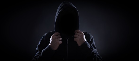Anonymous man in hood on black background. Banner design