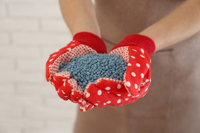 Photo of Woman holding pile of granular mineral fertilizer on blurred background, closeup