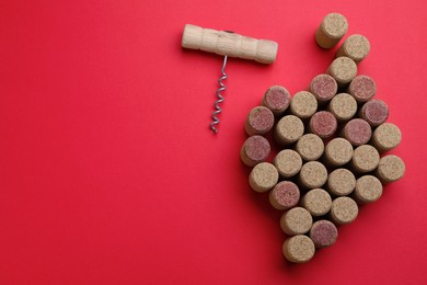 Photo of Grape of wine bottle stoppers and corkscrew on red background, flat lay. Space for text