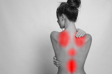 Woman suffering from back pain on light background, space for text