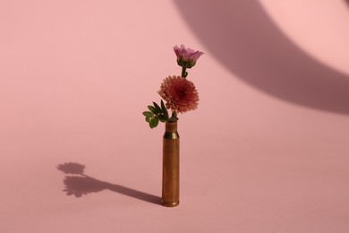 Photo of Bullet cartridge case and beautiful chrysanthemum flowers on pink background